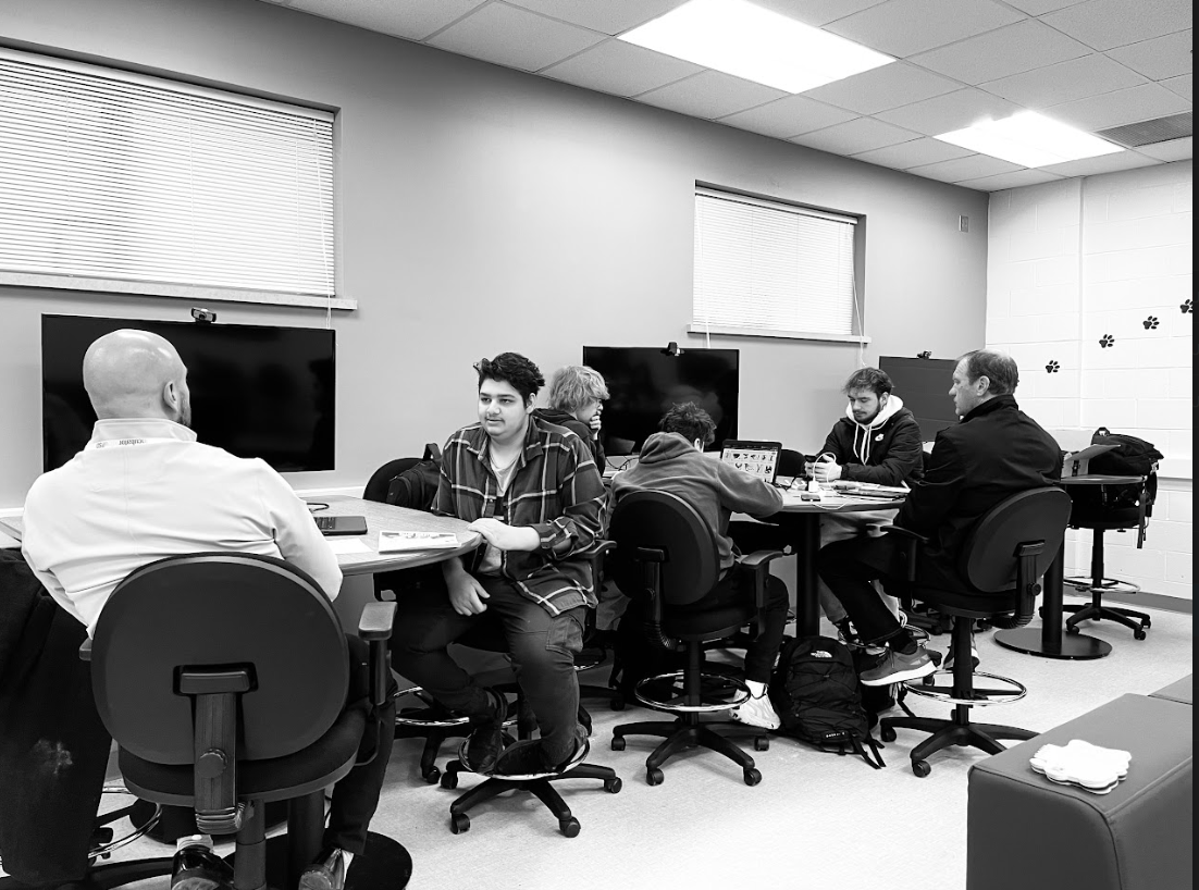 Ceo Mohamaad Ahmed discusses business experience with his mentor while the group behind him looks for different logos. This was taken Jan. 16 during first hour when the mentors speak to their groups during class about once a month.